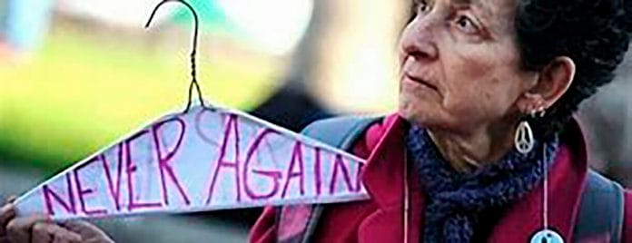 never again the coathanger Lady with coat hanger inscribed with words